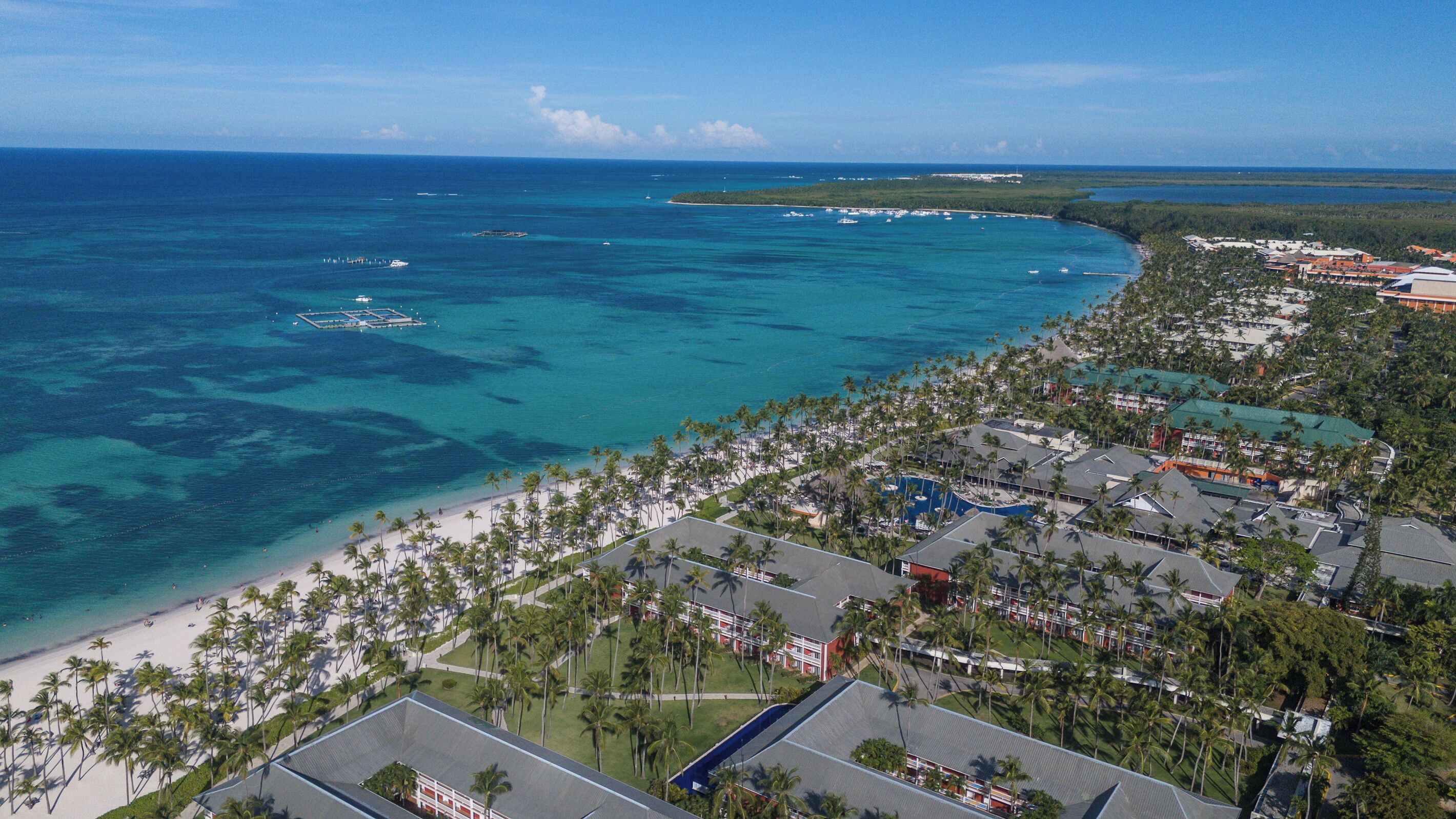 Um resort à beira-mar com praia, palmeiras e águas azul-claras.