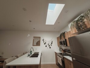 A modern kitchen with a skylight, stainless steel appliances, and a dining area with a white countertop. - Private Boho Tiny Home | Lakes, Wineries, Ski, Hike (Kelowna)
