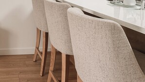 Une cuisine dotée d’un plan de travail blanc, d’un évier en acier inoxydable et de trois tabourets de bar avec des assises en osier tressé.