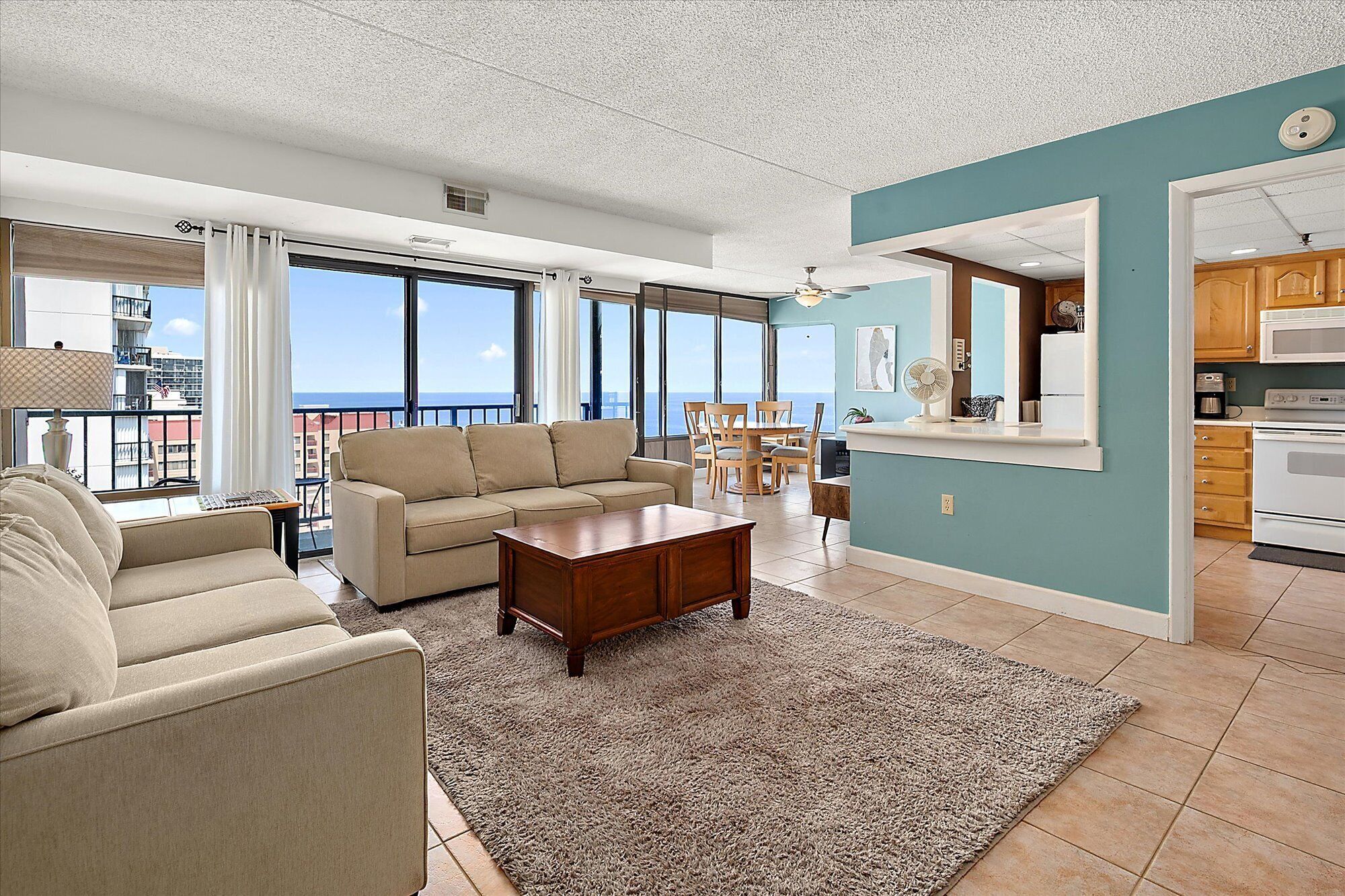A living room with a sofa, coffee table, and a view of the ocean through large windows.