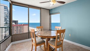 A balcony with a round table and chairs, a ceiling fan, and a view of the ocean and buildings. - 2 Bedroom Condo W/ View of Bay & Ocean (Ocean City)