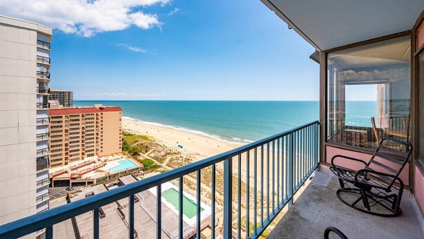 A balcony with a view of the beach and ocean, a pool, and a building with multiple floors. - 2 Bedroom Condo W/ View of Bay & Ocean (Ocean City)