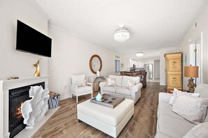 Ein modernes Wohnzimmer mit Kamin, weißen Sofas, einem Fernseher und einer Kristallleuchter.