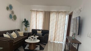 A living room with a sofa, coffee table, curtains, and a TV. - 3BR Ground Floor Villa with Spectacular Ocean View Rooftop Patio in La Romana (Villa Hermosa)