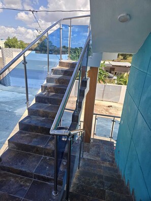 Un escalier avec des rampes en métal menant à un balcon d’où l’on peut admirer le ciel et les bâtiments.