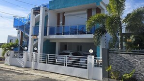 A modern two-story building with a balcony, a garage, and a stone wall. - 3BR Ground Floor Villa with Spectacular Ocean View Rooftop Patio in La Romana (Villa Hermosa)