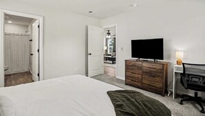 A bedroom with a bed, a dresser, a desk with a chair, a television, and a ceiling fan. - Whispering Waves in OIB! (Ocean Isle Beach)