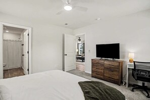 A bedroom with a bed, a dresser, a desk with a chair, a television, and a ceiling fan. - Whispering Waves in OIB! (Ocean Isle Beach)