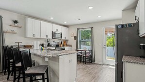 A modern kitchen with white cabinets, a granite countertop, and a built-in microwave. - Whispering Waves in OIB! (Ocean Isle Beach)