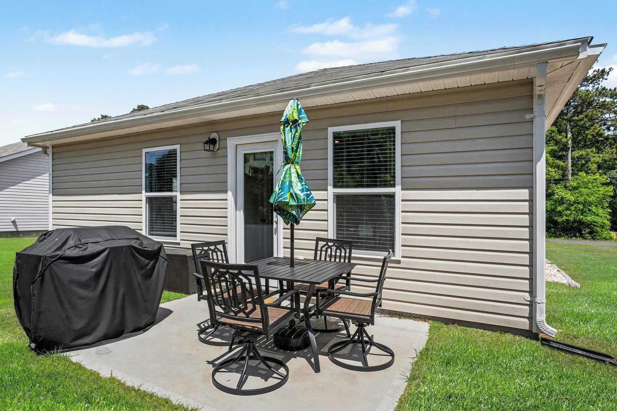 A single-story house with a covered patio area, a table with chairs, and a grill.