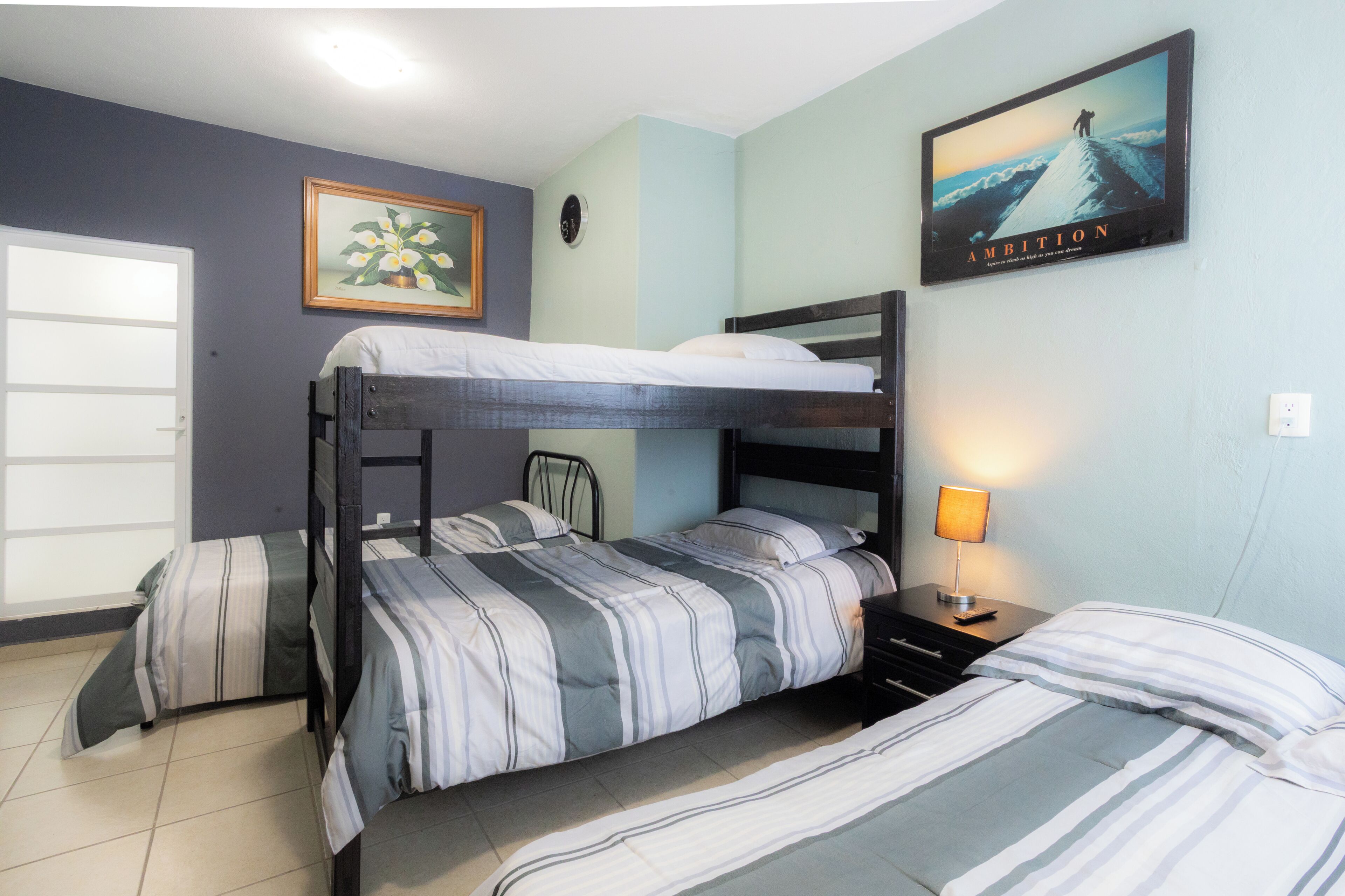 A bunk bed room with a painting, a clock, and a lamp on the nightstand.