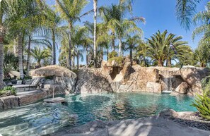 Un espace piscine agrémenté de palmiers, d’une cascade et de chaises longues.