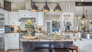 Une cuisine moderne avec des armoires blanches, un îlot en granit et des luminaires suspendus.