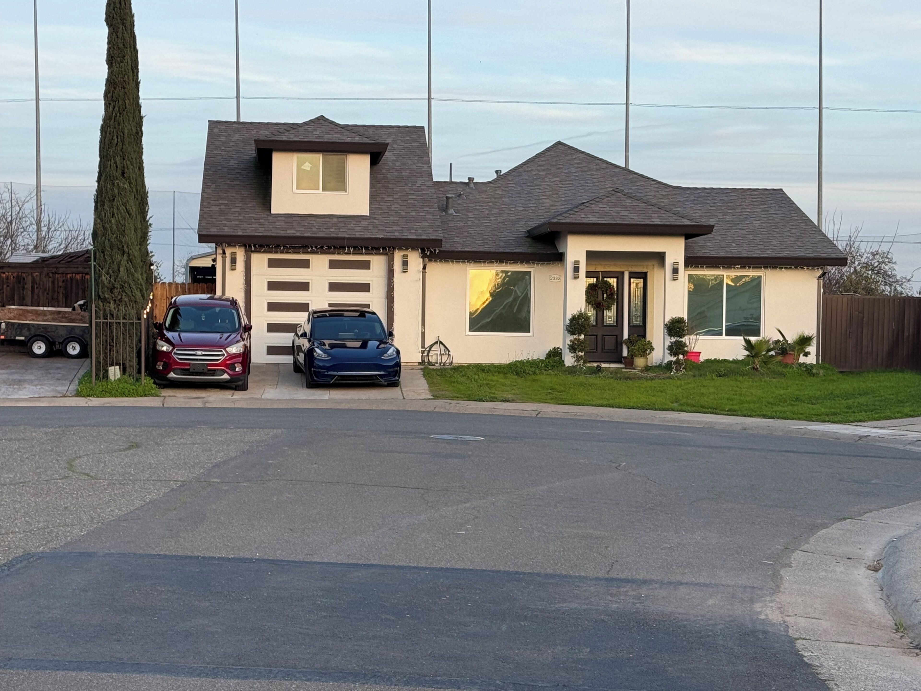 A two-story house with a garage, two cars parked in the driveway, and a well-maintained lawn.