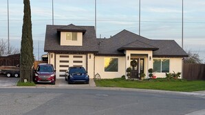 A two-story house with a garage, two cars parked in the driveway, and a well-maintained lawn. - Cozy Private Suite • Near SMF Airport (Elverta)