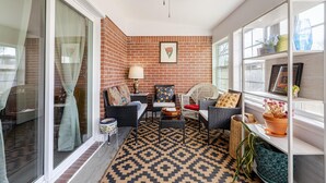 Una habitación con pared de ladrillo, ventilador de techo, alfombra estampada, muebles de mimbre y ventana con vistas.