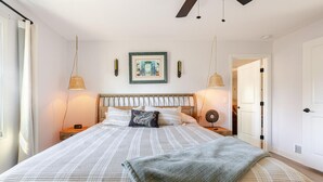 Un dormitorio con cama, mesitas de noche, ventilador de techo y un cuadro enmarcado en la pared.