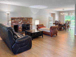 A living room with a brick fireplace, leather sofa, coffee table, dining table with chairs, and a chandelier.
