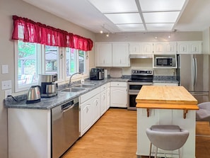 A modern kitchen with white cabinets, stainless steel appliances, a wooden island, and a red valance over the windows.