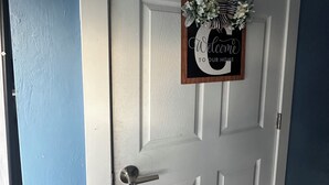 A white door with a 'Welcome to Our Home' sign and a small wreath. - Soothing studio with AC in lovely Naples, just minutes from the beach. (Naples)