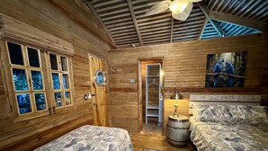 Eine Holzhütte mit zwei Betten, einer Holzbalkendecke, einer Tür zum Schlafzimmer und einem Vogelbild an der Wand.