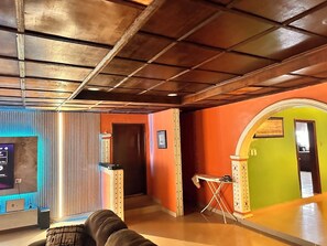 Quarto com teto de madeira, um balcão de recepção, uma pequena mesa e uma porta que dá para outro cômodo.