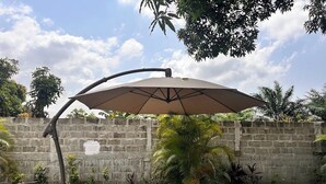A concrete patio with a large umbrella, surrounded by a low stone wall and various plants.