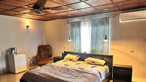 A bedroom with a bed, a chair, a nightstand, a desk, an air conditioner, and a ceiling fan.