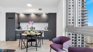 A modern kitchen with dark cabinets, a dining area with purple chairs, and a view of a high-rise building. - Premium 2BR Condo | Beautiful City View (Miami)