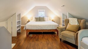 Een slaapkamer met een houten vloer, een bed met witte beddengoed, een stoel met hondentanddessin en een raam met uitzicht.