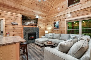 A wooden cabin interior with a fireplace, a stone wall, a sofa, and a bar area. - Amazing Getaway Pigeon Forge! Pool/HotTub/FirePit (Sevierville)