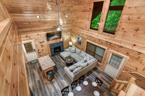 A wooden cabin interior with a living area, fireplace, and large windows. - Amazing Getaway Pigeon Forge! Pool/HotTub/FirePit (Sevierville)
