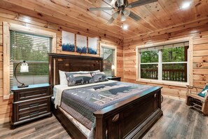 A wooden cabin bedroom with a bed, nightstands, a ceiling fan, and large windows. - Amazing Getaway Pigeon Forge! Pool/HotTub/FirePit (Sevierville)