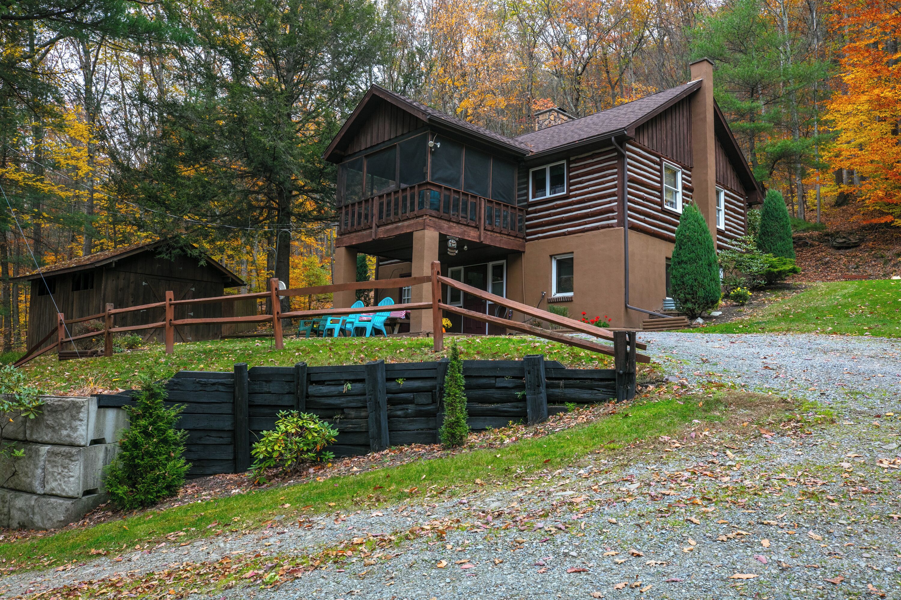 A cabin with a deck, surrounded by trees and a gravel path.