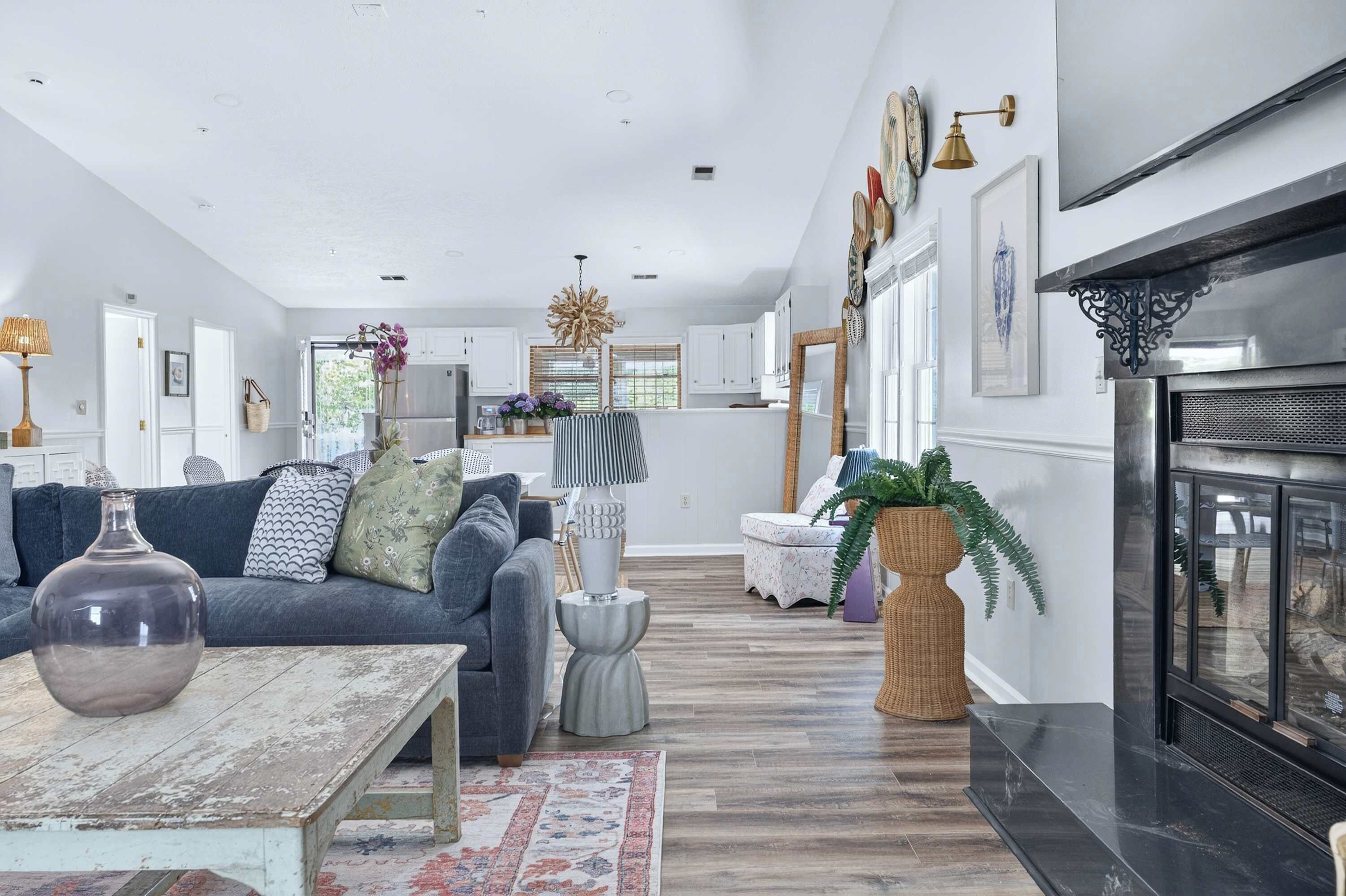A spacious living room with a fireplace, a dining area, and a kitchen in the background.