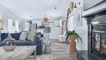 A spacious living room with a fireplace, a dining area, and a kitchen in the background.