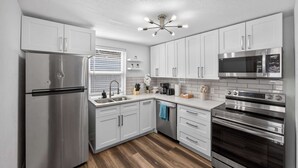 A modern kitchen with stainless steel appliances, white cabinetry, and a wooden floor.