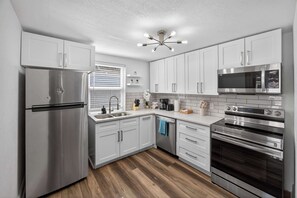 A modern kitchen with stainless steel appliances, white cabinetry, and a wooden floor. - Confort 2BR Near Top Attractions (Tampa)