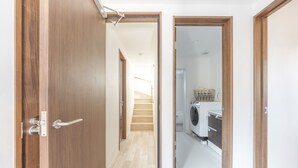 Un couloir menant à une cuisine équipée d’un lave-linge, avec un escalier et des portes en bois.