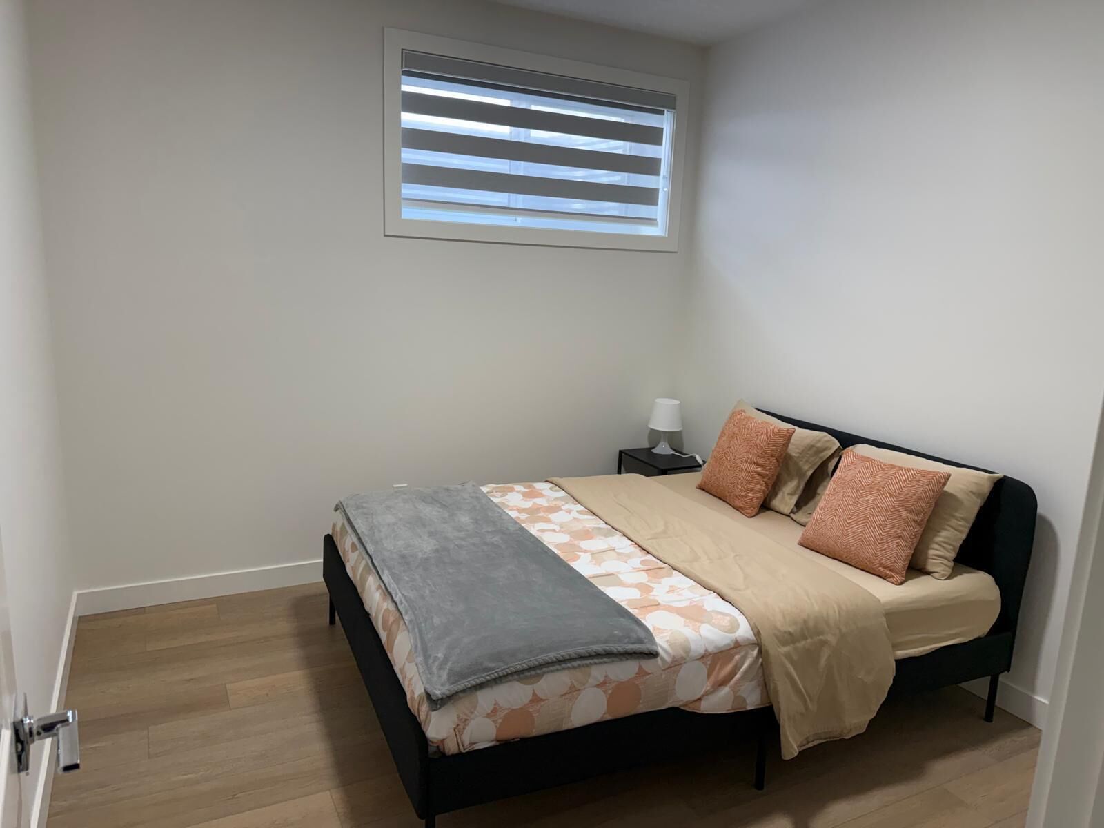 A bedroom with a bed, a nightstand, a lamp, and a window with blinds.
