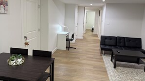 Een moderne woonkamer met een donkerhouten eettafel, een zwarte bank en een wit bureau met een lamp.