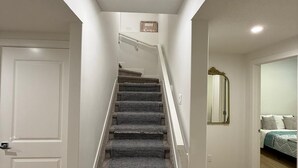 Een trap met beklede treden die uitkomt op een plateau, witte wanden en een deur aan de linkerkant.