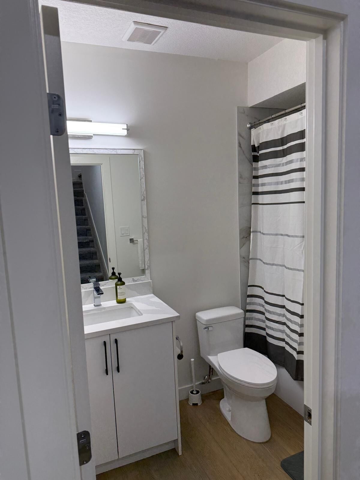 Un bany amb un vàter blanc, un lavabo amb mirall i una cortina de bany a ratlles.