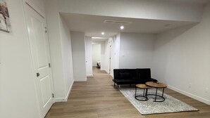 Een hal met houten vloer, een zwarte bank en een kleine ronde tafel met vloerkleed.