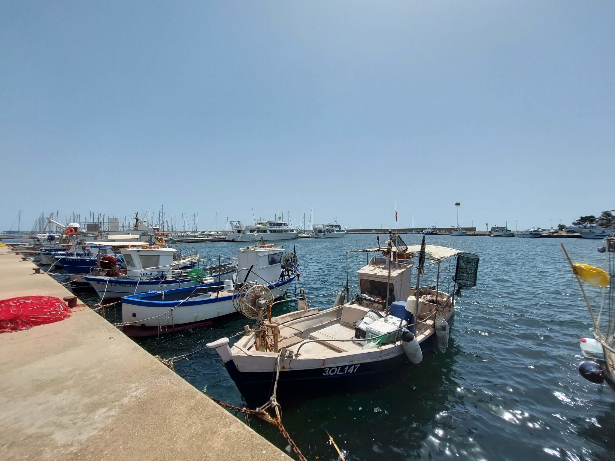 Um porto com vários barcos atracados, um cais de concreto e um céu azul límpido.