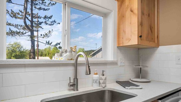 Eine Küche mit einem Edelstahlspülbecken, einem Fenster mit Blick auf Bäume und Holzschränken.