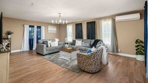 Ein Wohnzimmer mit grauem Sofa, einem gemusterten Sessel, einem Couchtisch und einer Chandelier.