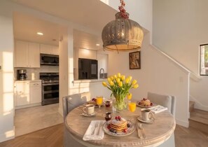 Eine moderne Küche mit Edelstahlgeräten, ein Essbereich mit rundem Tisch, gedeckt für das Frühstück, und eine Treppe, die zu einer weiteren Ebene führt.