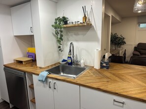 Una cucina con lavastoviglie, lavello, piano di lavoro in legno, una pianta pensile e un piccolo ripiano con oggetti.