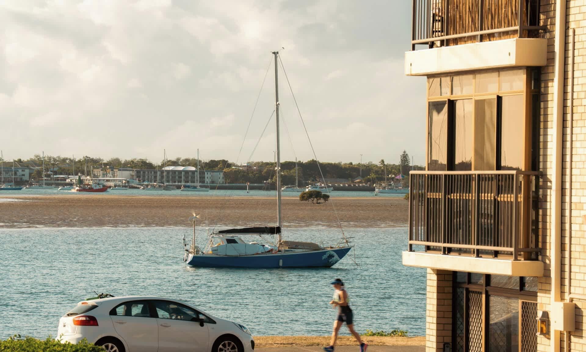 Une vue sur le bord de l’eau, avec un bateau, une voiture et un immeuble doté d’un balcon.